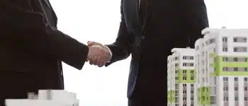 תמונת אווירה אנשי עסקים לוחצים ידים מאחורי דגם בניין