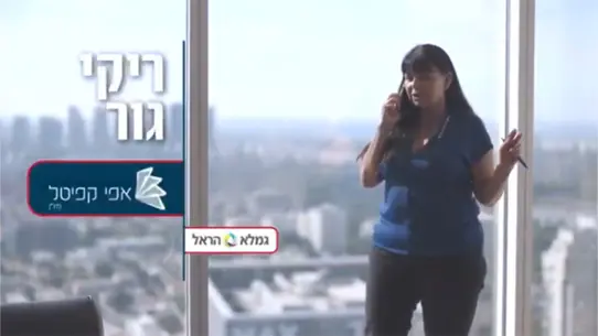 ריקי גור אפי קפיטל. משוחחת בטלפון מתוך בניין משרדים